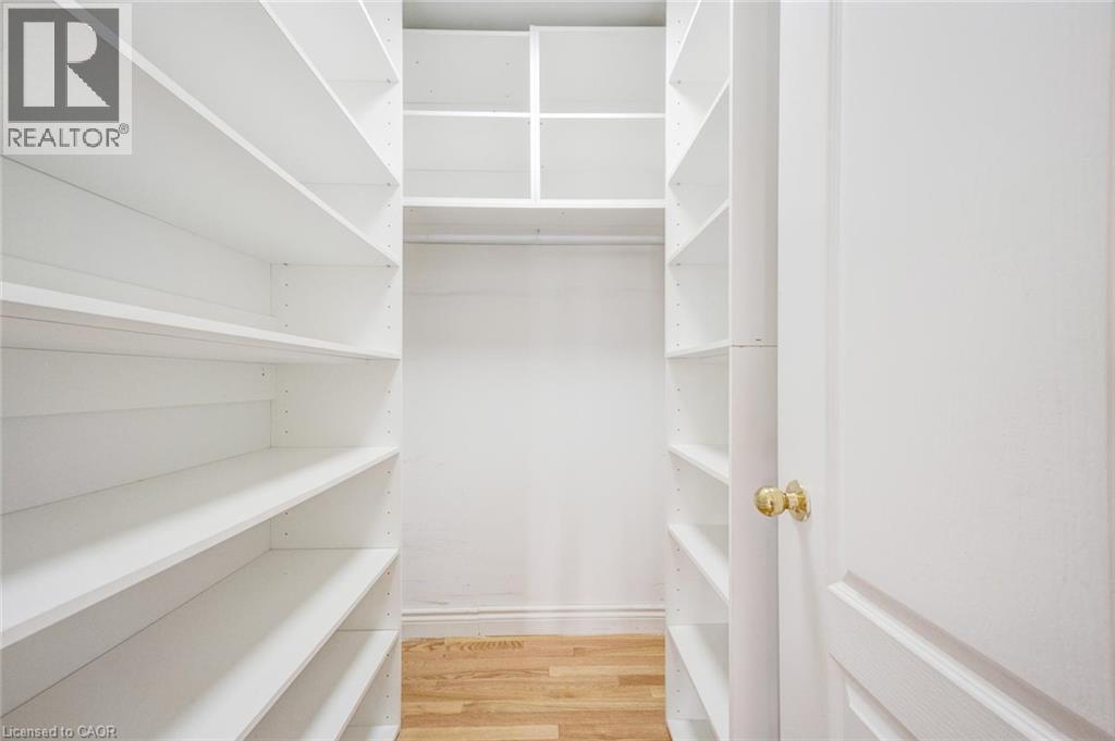 Walk-in closet featuring extensive built-in white shelving, upper storage compartments, and wood-finish flooring - 5 Freshspring Drive, Brampton, ON - Indoor With Storage