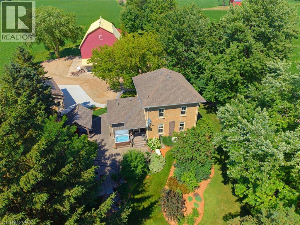 Expansive property featuring a multi-story brick residence, a red barn with a yellow roof, a covered outdoor spa, and a stone patio - 8430 Road 146, Listowel, ON - Outdoor