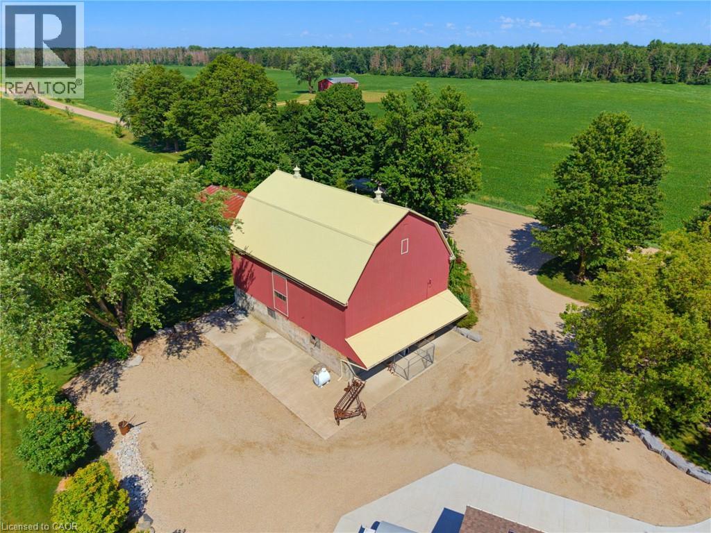 Red barn structure featuring a gambrel roof with a light-colored metal finish, concrete foundation, and an attached covered lean-to area - 8430 Road 146, Listowel, ON - Outdoor With View