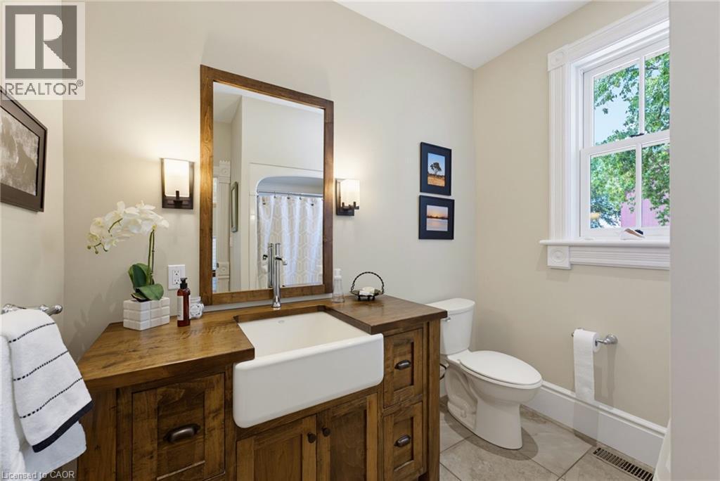 Bathroom featuring a wood-finish vanity with an integrated farmhouse sink, framed mirror, and wall sconces - 8430 Road 146, Listowel, ON - Indoor Photo Showing Bathroom