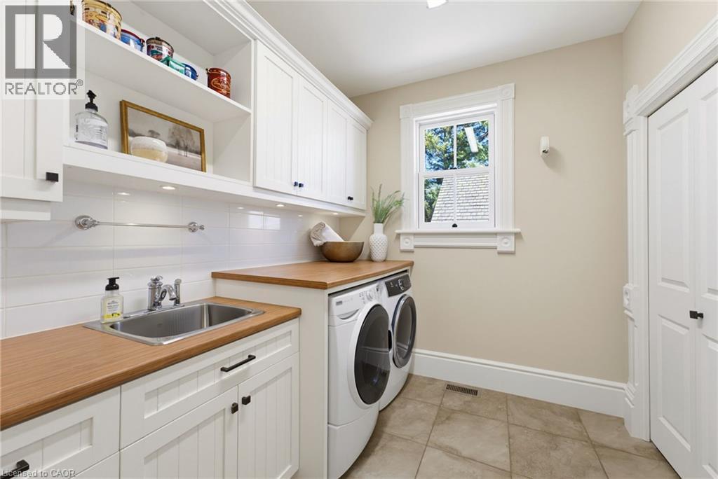 Laundry area featuring wood-finish countertops, white shaker cabinetry with black hardware, and a stainless steel sink - 8430 Road 146, Listowel, ON - Indoor Photo Showing Laundry Room