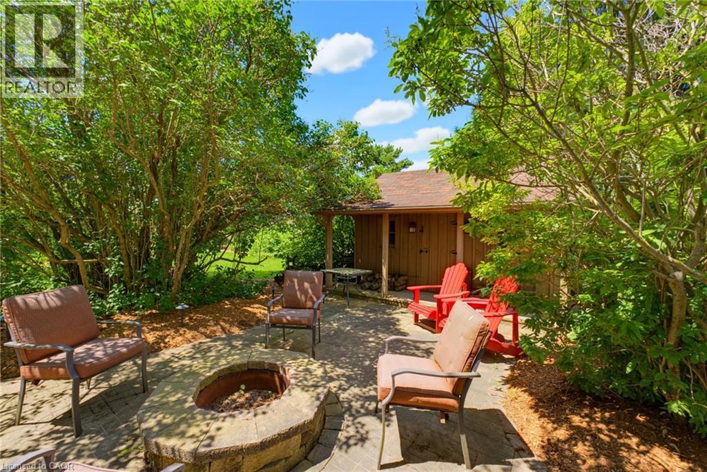 Stone-paver patio featuring a built-in stone fire pit, surrounded by lush mature trees and plantings - 8430 Road 146, Listowel, ON - Outdoor