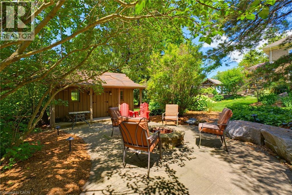 Stone patio featuring a built-in fire pit, surrounded by lush landscaping and mature trees - 8430 Road 146, Listowel, ON - Outdoor