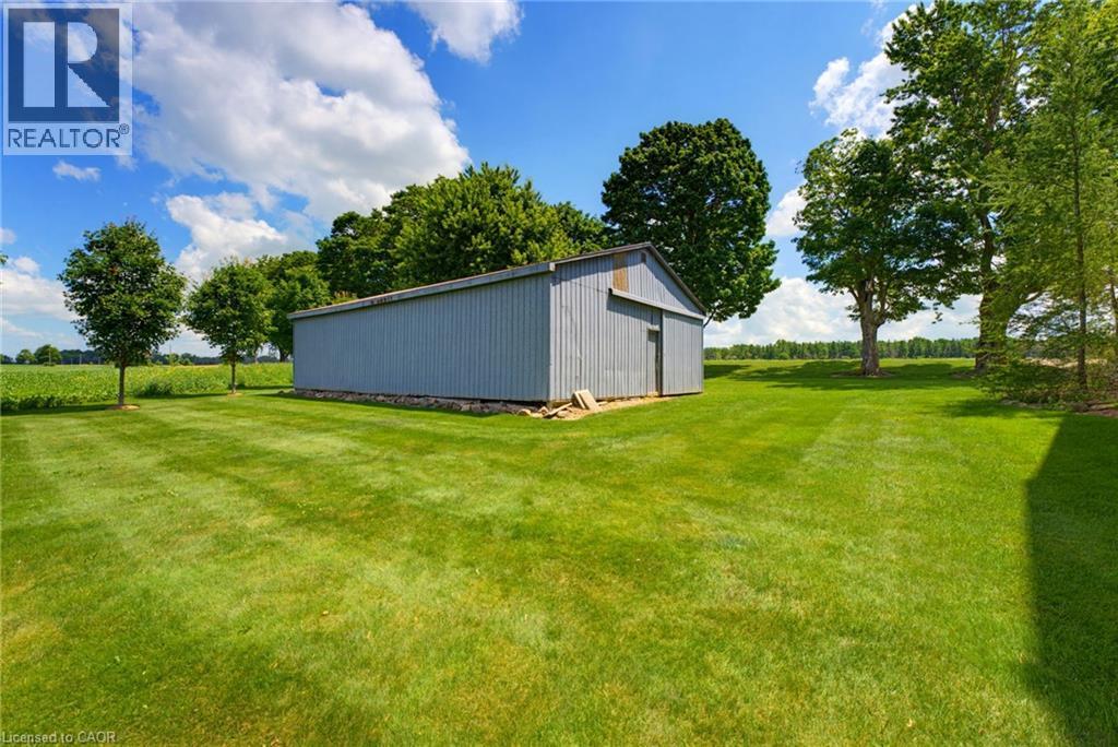 Expansive green lawn featuring a corrugated metal outbuilding with a sliding door, established shade trees, and clear sky overhead - 8430 Road 146, Listowel, ON - Outdoor