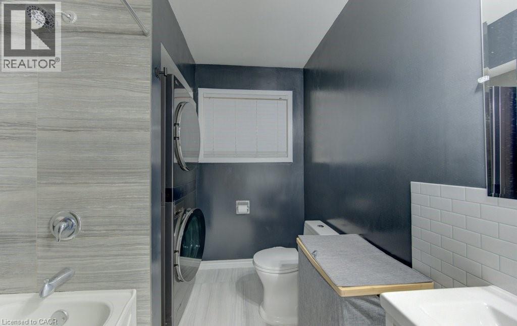 Bathroom featuring a shower-tub combination, a stackable washer and dryer, a toilet, and a vanity with a rectangular sink - 136 Dunsmere Drive, Kitchener, ON - Indoor Photo Showing Bathroom