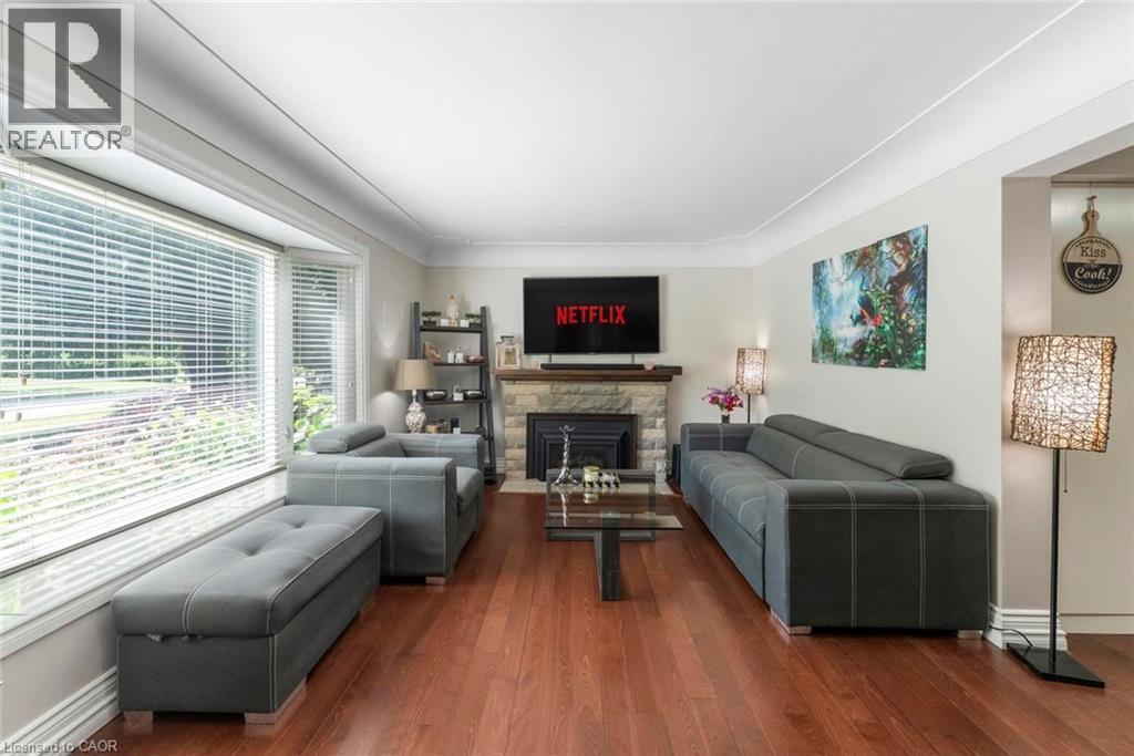 Spacious living area featuring rich wood-finish flooring, a stone-clad fireplace, and a built-in shelving unit - 1063 Joan Drive, Burlington, ON - Indoor Photo Showing Living Room With Fireplace