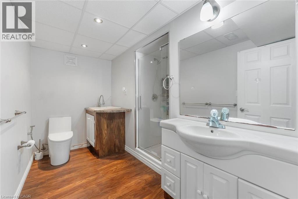 Spacious bathroom featuring a glass-enclosed shower, two vanities, and wood-finish flooring - 1063 Joan Drive, Burlington, ON - Indoor Photo Showing Bathroom