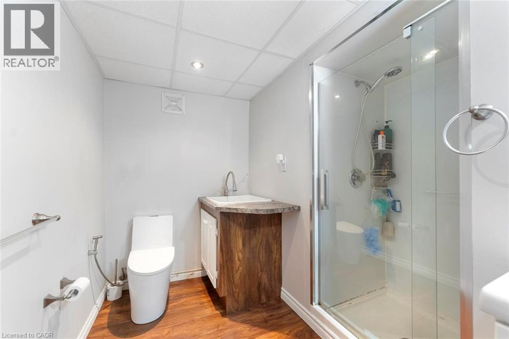 Three-piece bathroom featuring a glass-enclosed shower, wood-finish flooring, a contemporary vanity with an integrated sink, a white commode, and recessed ceiling lighting - 1063 Joan Drive, Burlington, ON - Indoor Photo Showing Bathroom