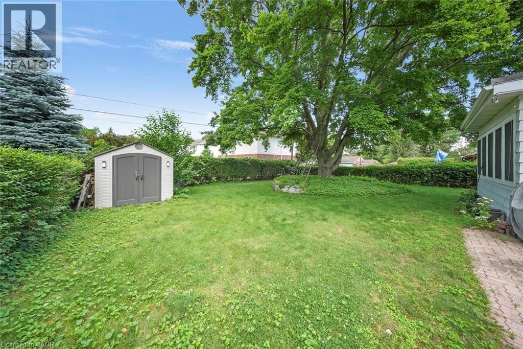 Expansive rear yard featuring mature trees, a manicured lawn, and a contemporary storage shed with dual gray doors and exterior lighting - 1063 Joan Drive, Burlington, ON - Outdoor