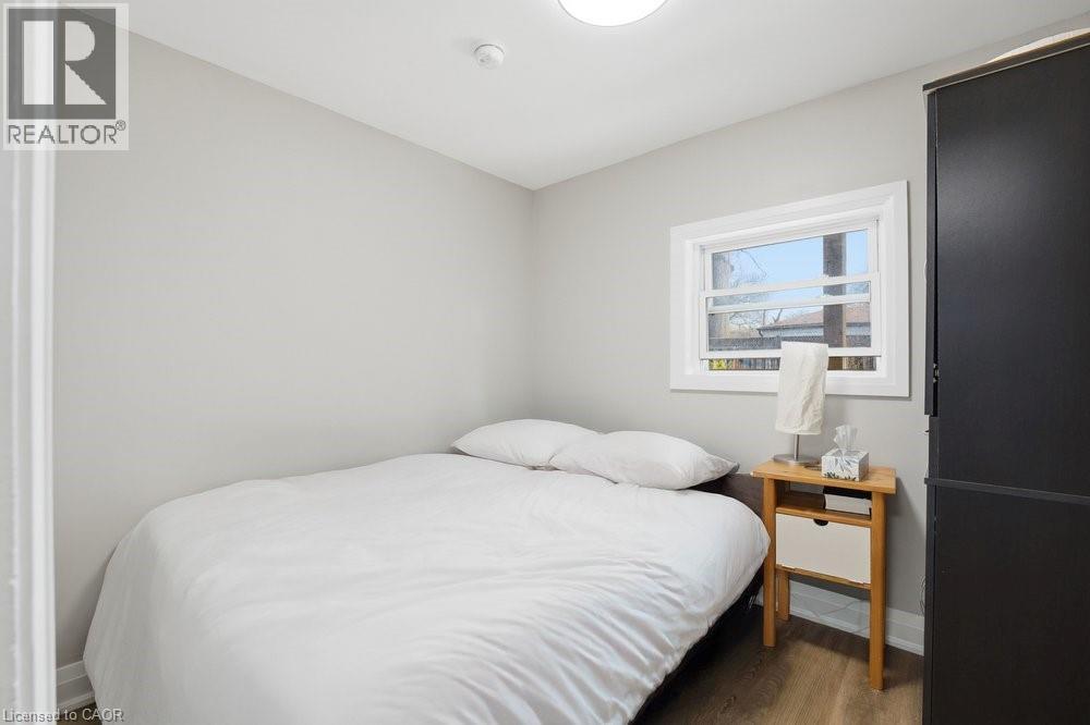 Compact room featuring light gray walls, wood-finish flooring, a white-trimmed window, a flush-mount ceiling light, and a dark built-in wardrobe - 773 Lawrence Road, Hamilton, ON - Indoor Photo Showing Bedroom