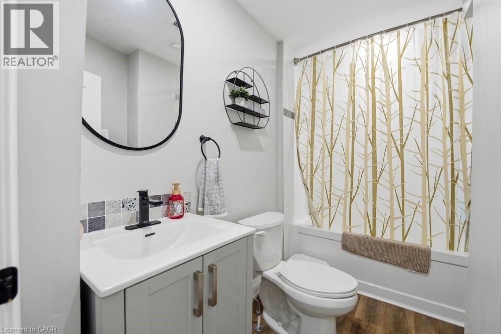 Bathroom featuring a light gray vanity with a white integrated sink, a matte black single-handle faucet, and a black-framed oval mirror - 773 Lawrence Road, Hamilton, ON - Indoor Photo Showing Bathroom