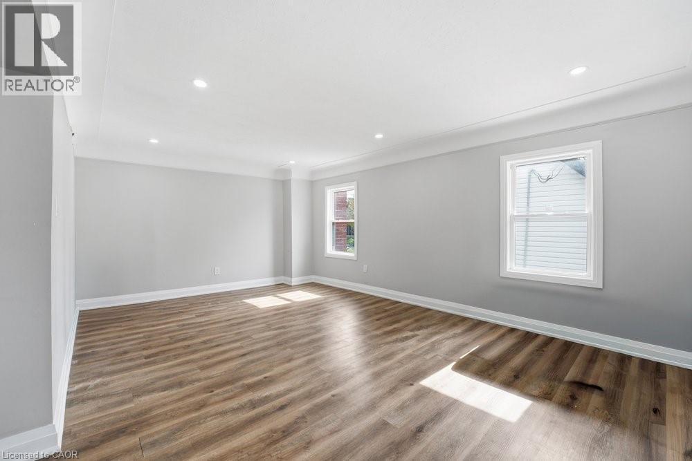 Spacious room featuring wood-finish flooring, light grey walls, recessed ceiling lighting, crown molding, and two windows with white trim - 773 Lawrence Road, Hamilton, ON - Indoor Photo Showing Other Room