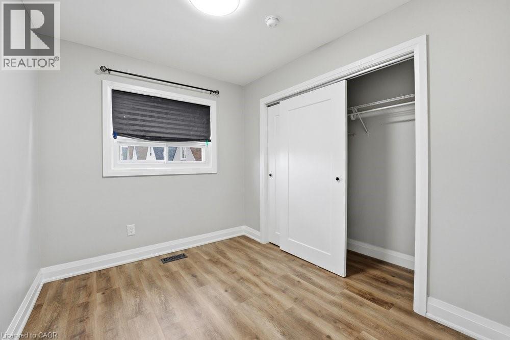 Room featuring wood-finish flooring, a window with a dark blind, a flush mount ceiling light, light gray painted walls, and a closet with white sliding doors and interior shelving - 773 Lawrence Road, Hamilton, ON - Indoor Photo Showing Other Room