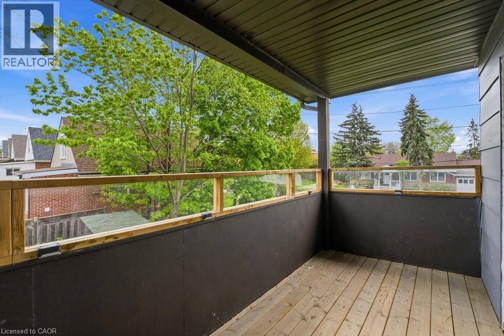 Covered outdoor patio featuring wood-finish flooring, a wood and glass panel railing, and a dark-paneled lower wall - 773 Lawrence Road, Hamilton, ON - Outdoor With Exterior
