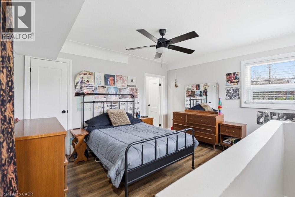 Bedroom featuring wood-finish flooring, a ceiling fan with integrated lighting, a white framed window with blinds, a white interior door with black hardware, and light-colored wall paint - 773 Lawrence Road, Hamilton, ON - Indoor Photo Showing Bedroom