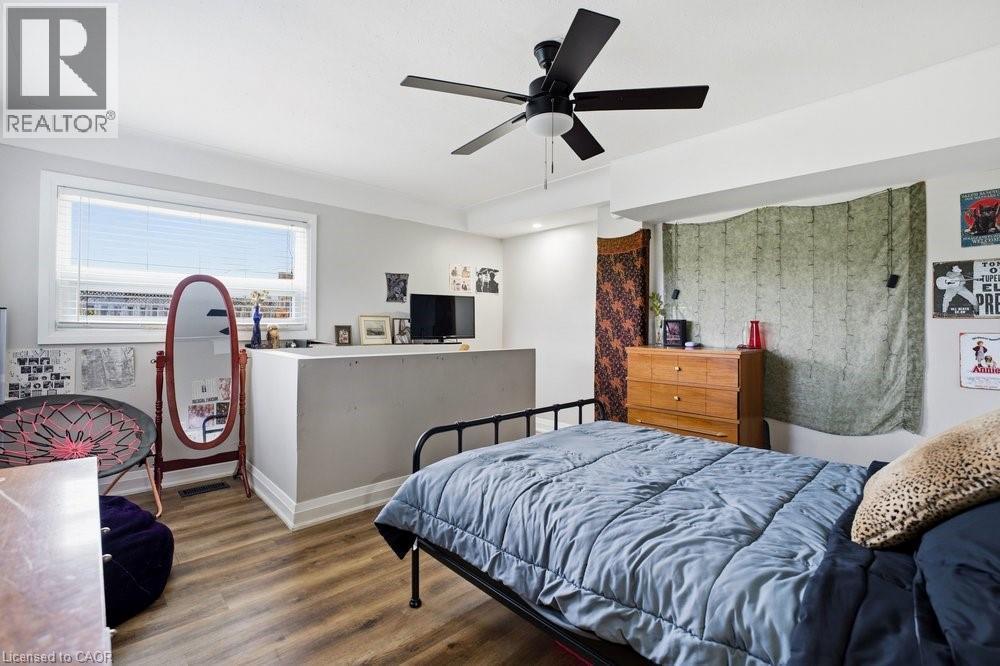 Spacious room featuring wood-finish flooring, a contemporary ceiling fan, and a wide window with horizontal blinds - 773 Lawrence Road, Hamilton, ON - Indoor Photo Showing Bedroom