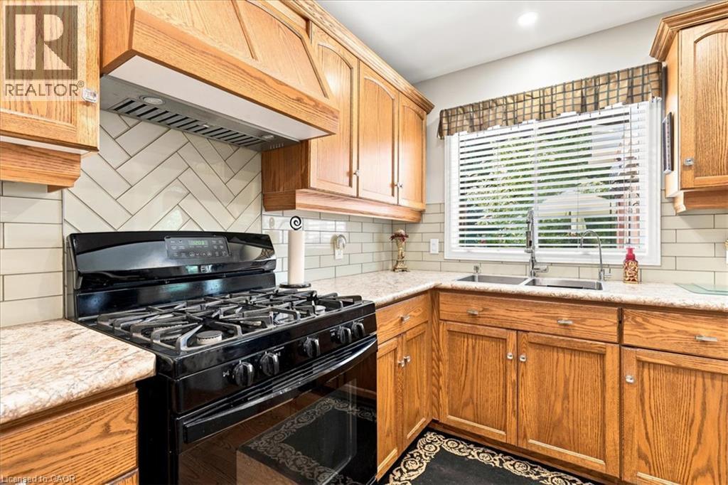 Kitchen featuring a black gas range, wood cabinetry, light-toned countertops, and a herringbone tile backsplash - 39 Everwood Run, Kitchener, ON - Indoor Photo Showing Kitchen With Double Sink