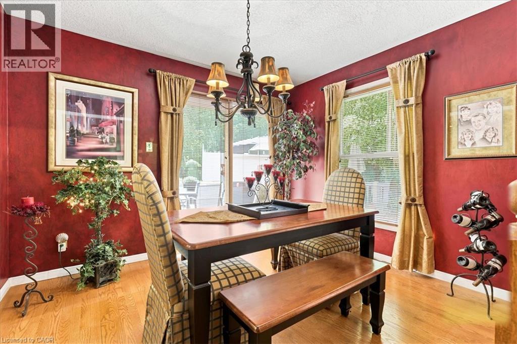 Dining area featuring wood-finish flooring, a contemporary chandelier, red wall treatment, and windows with blinds and drapes - 39 Everwood Run, Kitchener, ON - Indoor Photo Showing Dining Room