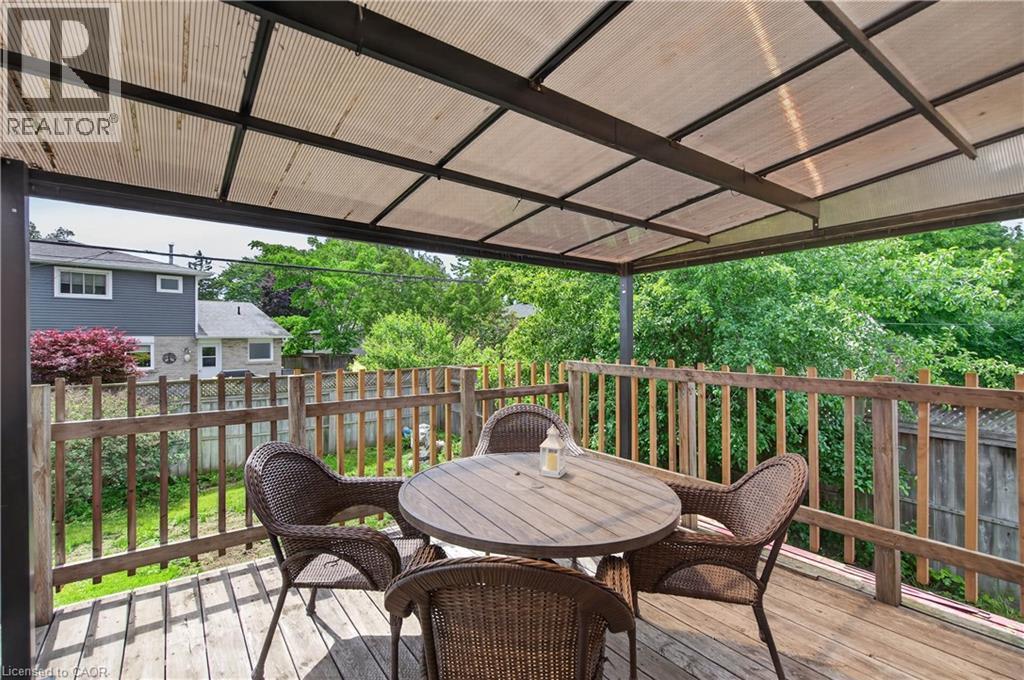 Spacious outdoor deck featuring wood-finish railing and flooring, covered by a translucent panel awning with a dark metal frame - 236 Hammersmith Court, Burlington, ON - Outdoor With Deck Patio Veranda With Exterior