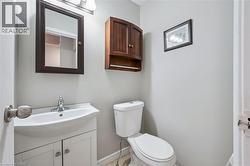Compact bathroom featuring a white toilet, pedestal sink with vanity, wall-mounted mirror, and wood-finish wall cabinet - 