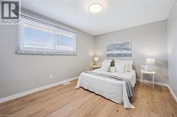 Light-filled room featuring wood-finish flooring, a large window with white blinds, neutral wall paint, white baseboards, and a flush-mount ceiling light - 
