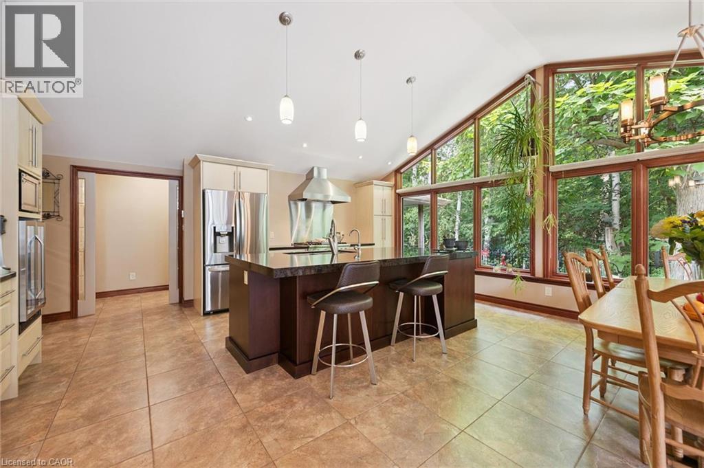 Kitchen and dining area featuring large format tile flooring, a dark wood-finish island with integrated seating, stainless steel appliances, and extensive window walls with wood trim, featuring large - 410 Avenue Road, Cambridge, ON - Indoor