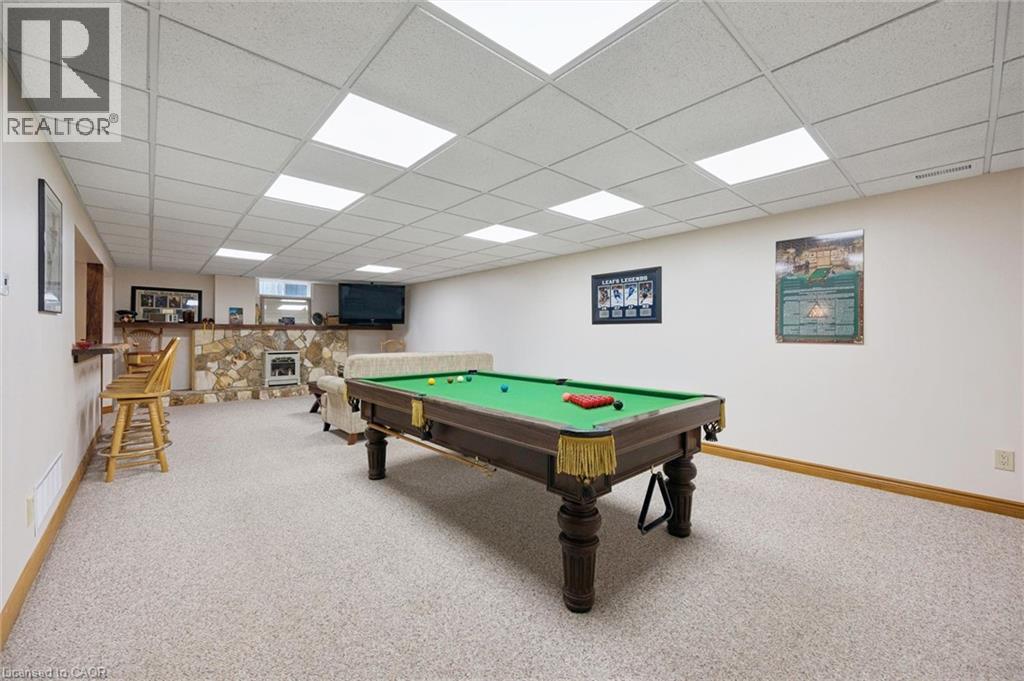 Spacious entertainment area featuring a drop ceiling with integrated lighting, a stone-clad hearth, a built-in bar, and neutral Berber carpeting - 410 Avenue Road, Cambridge, ON - Indoor Photo Showing Other Room