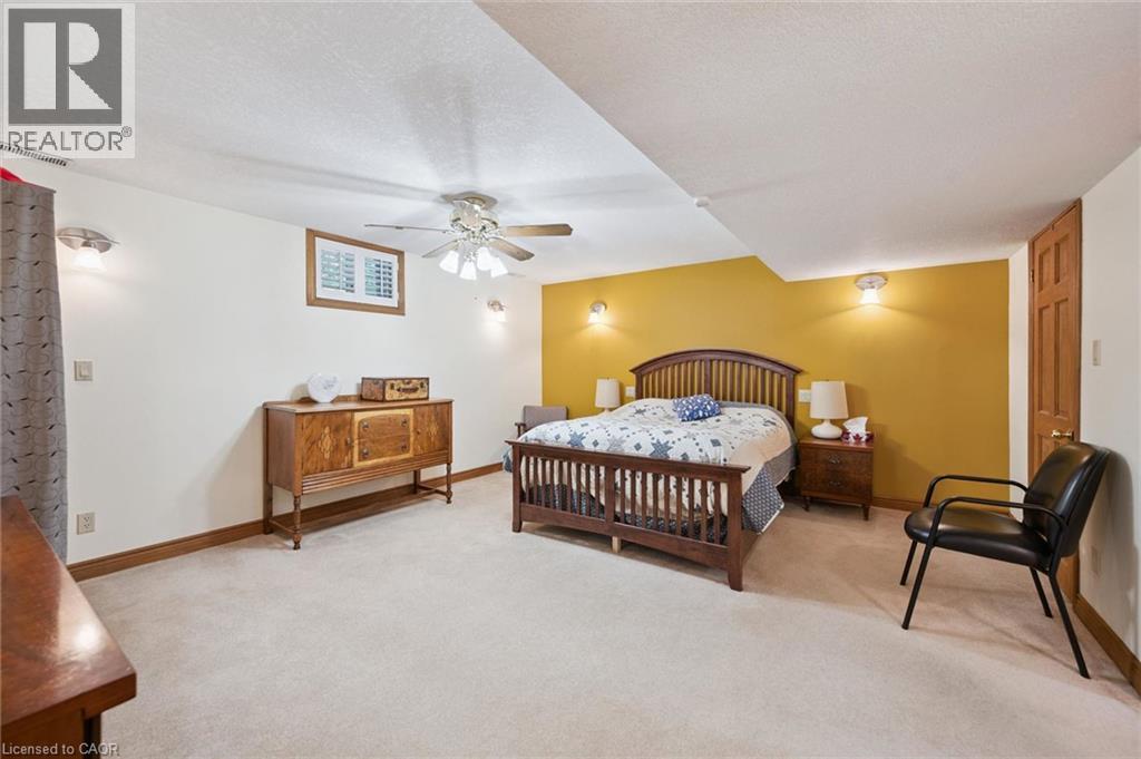 Carpeted room featuring a ceiling fan with integrated lighting, wall sconces, wood-trim baseboards, and all doors are solid oak wood six panel - 410 Avenue Road, Cambridge, ON - Indoor Photo Showing Bedroom