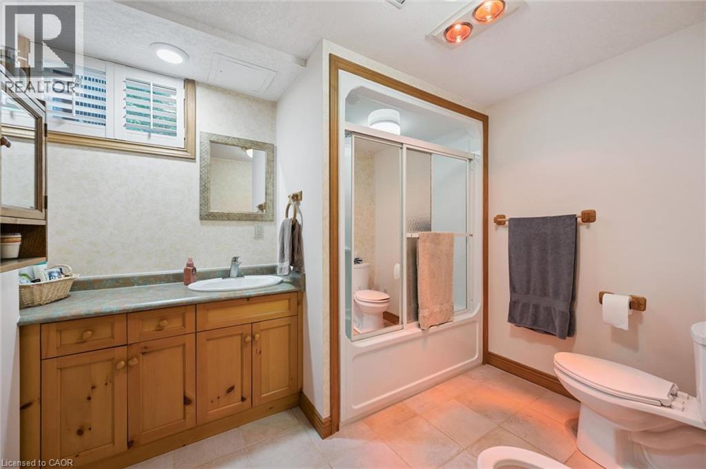 Bathroom featuring a natural wood vanity with a single basin sink, a framed mirror, and a shower-tub combination with sliding glass doors, an integrated IR style overhead heat light and a bidet - 410 Avenue Road, Cambridge, ON - Indoor Photo Showing Bathroom