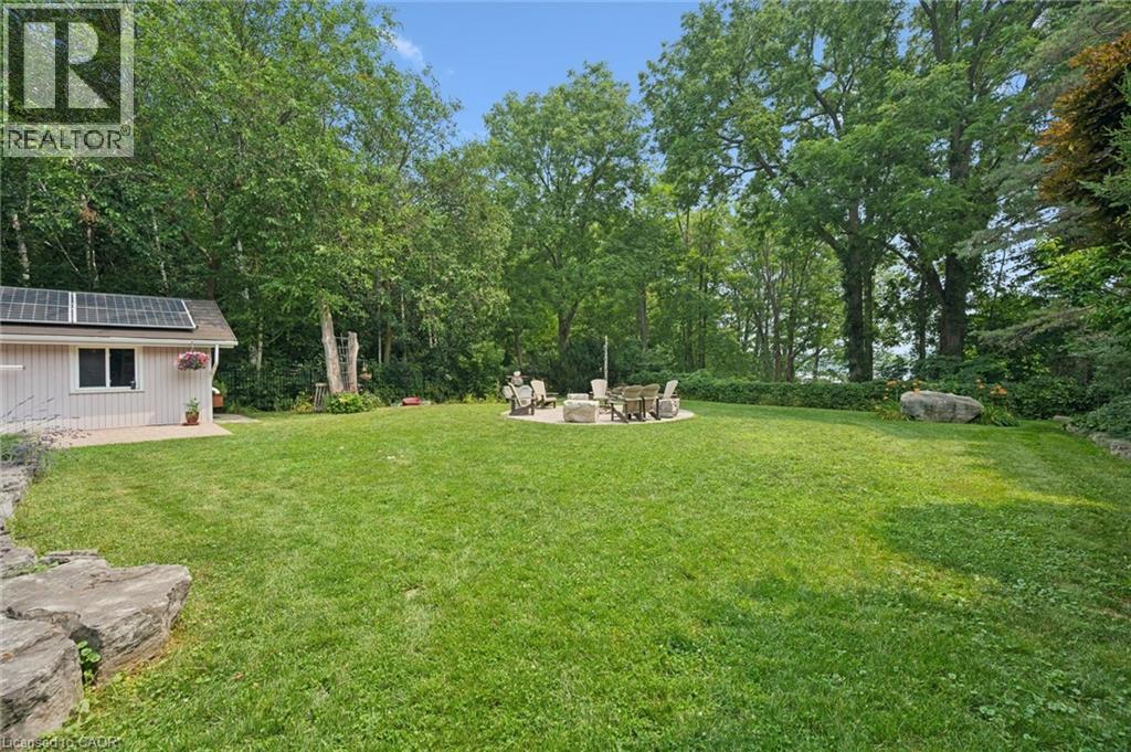 Expansive green lawn featuring a stone patio, mature trees, and a detached structure with solar panels, irrigation system - 410 Avenue Road, Cambridge, ON - Outdoor