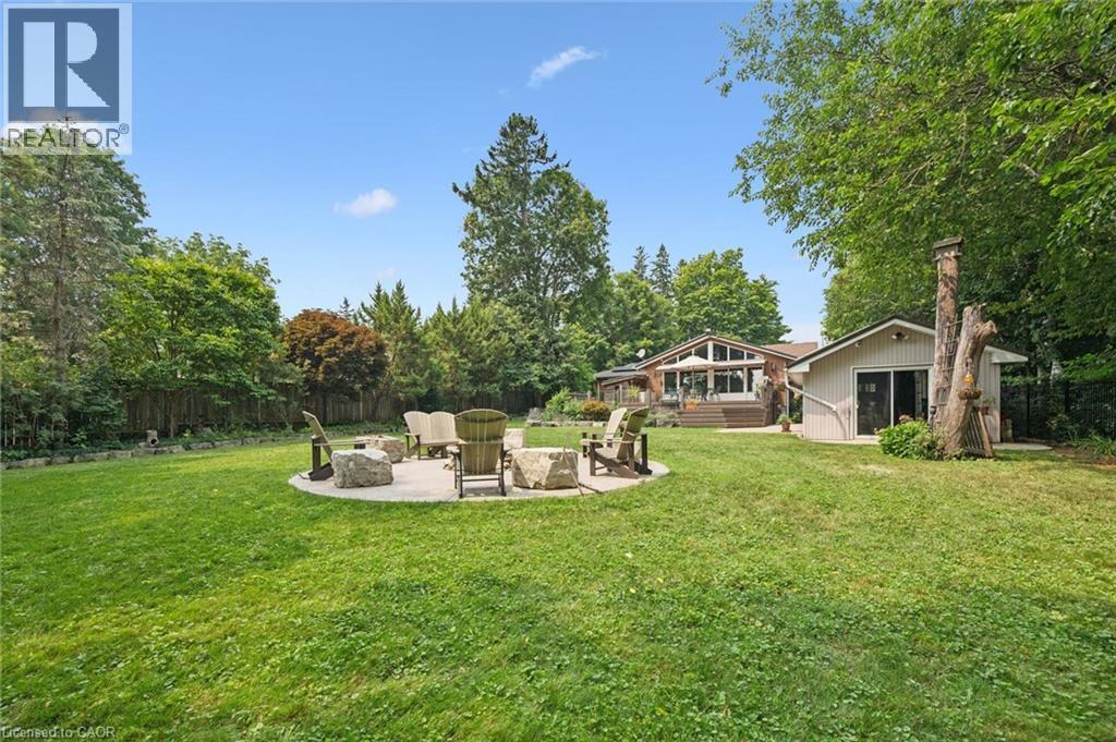 Expansive backyard featuring a large lawn, a stone patio with a fire pit, mature trees, a detached outbuilding with sliding glass doors, and a multi-level deck on the main residence, irrigation system - 410 Avenue Road, Cambridge, ON - Outdoor