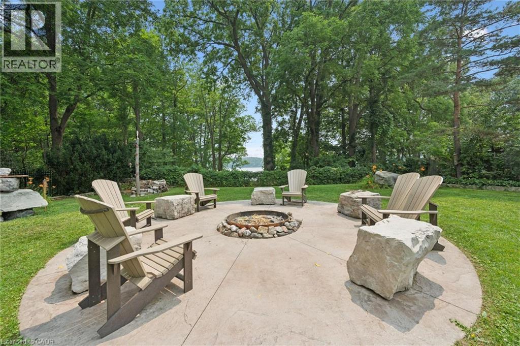 Circular concrete patio with a central stone-ringed fire pit, surrounded by Adirondack-style chairs and natural stone seating, with an Inukshuk stone feature - 410 Avenue Road, Cambridge, ON - Outdoor
