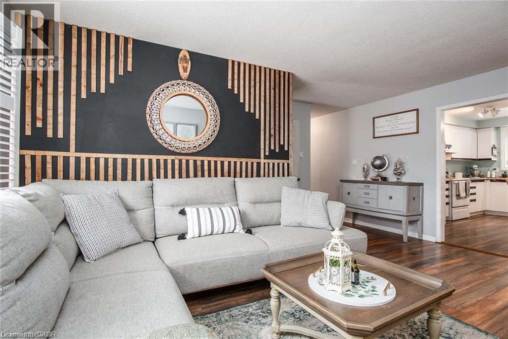 Living area with wood-finish flooring and a striking accent wall featuring a geometric wood slat design on a dark backdrop - 67 Pinemeadow Crescent, Waterloo, ON - Indoor Photo Showing Living Room