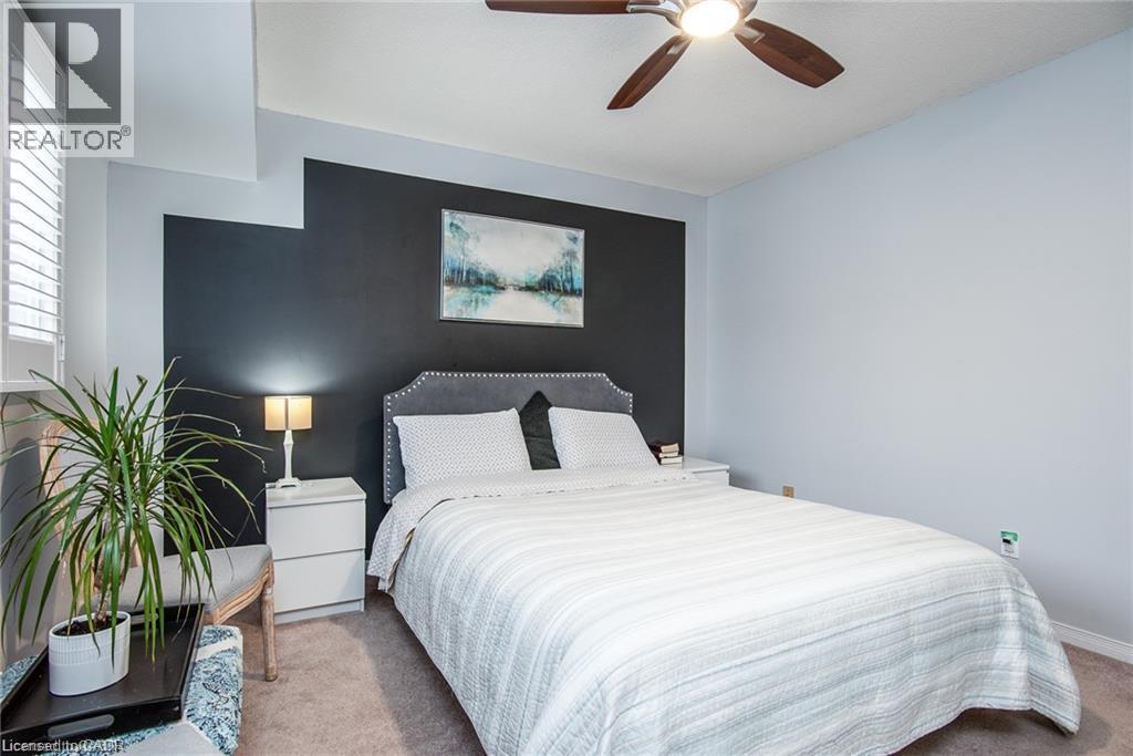 Bedroom featuring a ceiling fan with integrated lighting, a contrasting accent wall, plantation shutters, and soft carpeting - 67 Pinemeadow Crescent, Waterloo, ON - Indoor Photo Showing Bedroom