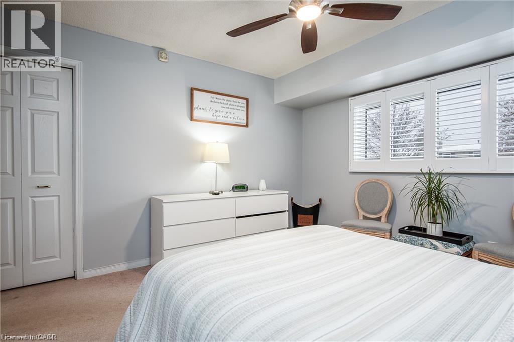 Bedroom featuring a ceiling fan with integrated lighting, a full-wall window with white plantation shutters, and a double-panel bifold closet door - 67 Pinemeadow Crescent, Waterloo, ON - Indoor Photo Showing Bedroom