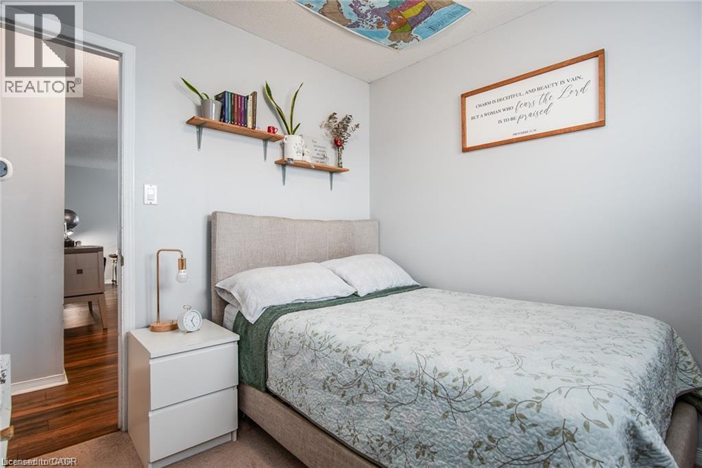 Carpeted bedroom featuring a neutral color palette, a visible doorway to a wood-finish floor, and built-in wall shelves - 67 Pinemeadow Crescent, Waterloo, ON - Indoor Photo Showing Bedroom