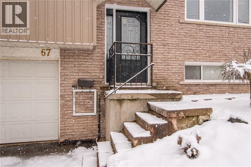 Brick facade with a white garage door, concrete steps, and a black wrought iron handrail - 67 Pinemeadow Crescent, Waterloo, ON - Outdoor With Exterior