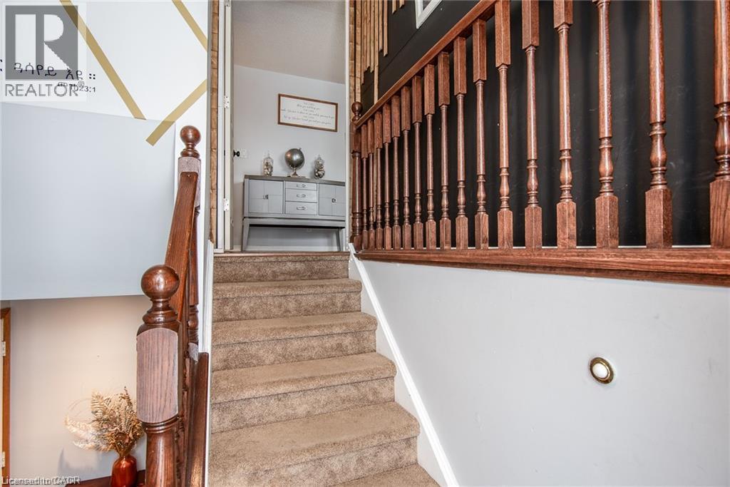 Carpeted staircase featuring a wood-finish handrail and balusters, with a contemporary built-in wall light - 67 Pinemeadow Crescent, Waterloo, ON - Indoor Photo Showing Other Room