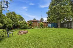 Expansive green lawn with a brick fire pit, mature trees, and a wooden privacy fence -