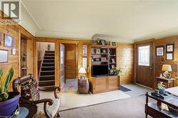 Living area featuring wood paneling throughout, a staircase with dark treads, a wood-finish entry door with decorative glass, and light-colored carpeting -