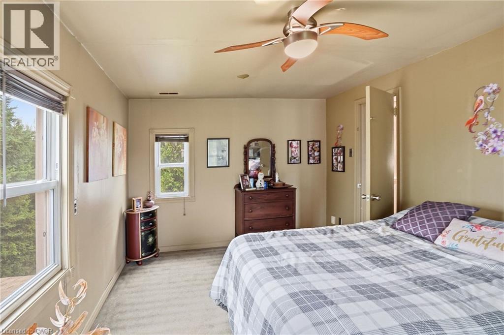 Carpeted room featuring multiple windows with tree-lined exterior, light-toned walls, and a ceiling fan with integrated lighting - 834 Mohawk Road E, Hamilton, ON - Indoor Photo Showing Bedroom