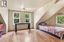 Attic space featuring wood-finish flooring, multiple windows, and angled ceilings -