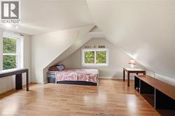 Attic room featuring light wood-finish flooring, white walls, and a sloped ceiling -