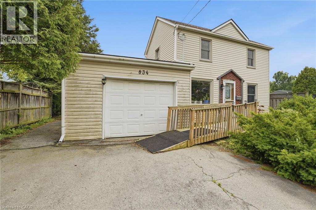 Two-story residence with light-toned siding, attached single-car garage, and a wooden access ramp leading to the main entry - 834 Mohawk Road E, Hamilton, ON - Outdoor