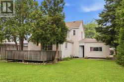Expansive grassy yard featuring a wooden deck with railing, mature trees, and a privacy fence -