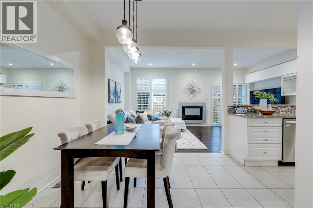 Combined kitchen, dining, and living areas featuring white tiled flooring, a linear pendant light fixture, a built-in fireplace, and a kitchen island with a mosaic tile backsplash - 598 Bessborough Drive, Milton, ON - Indoor Photo Showing Dining Room With Fireplace