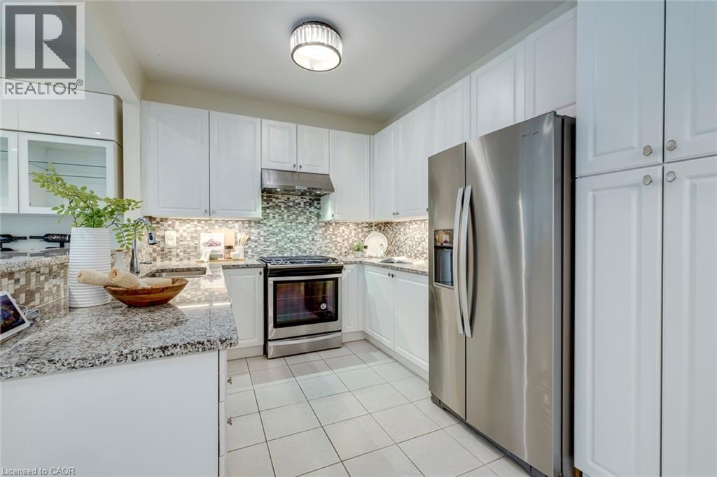 Kitchen featuring white cabinetry, stainless steel appliances, granite countertops, a mosaic tile backsplash, and tile flooring - 598 Bessborough Drive, Milton, ON - Indoor Photo Showing Kitchen With Upgraded Kitchen