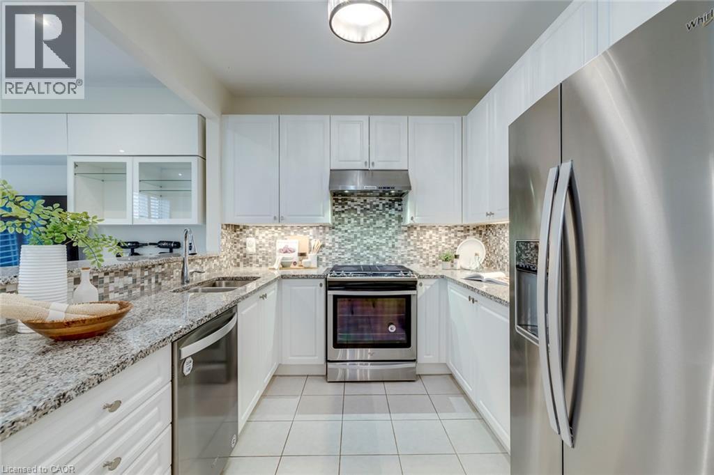 Contemporary kitchen featuring white cabinetry, stainless steel appliances, speckled countertops, a mosaic tile backsplash, and light tile flooring - 598 Bessborough Drive, Milton, ON - Indoor Photo Showing Kitchen With Double Sink With Upgraded Kitchen
