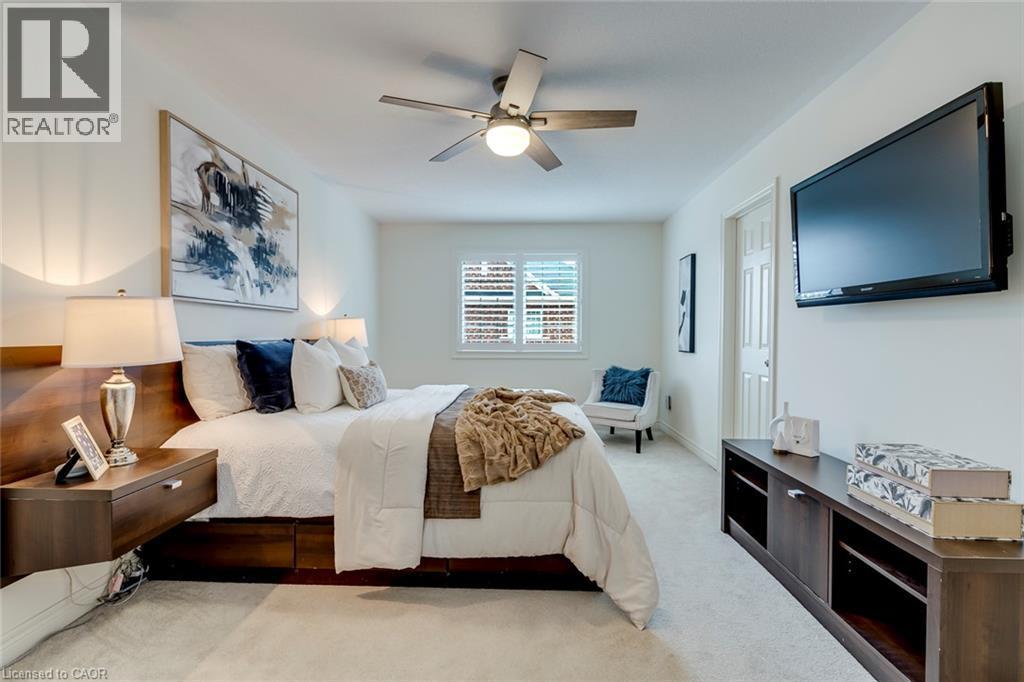 Bedroom featuring neutral wall colors, carpet flooring, a window with plantation shutters, a ceiling fan with integrated lighting, and a built-in media console - 598 Bessborough Drive, Milton, ON - Indoor Photo Showing Bedroom