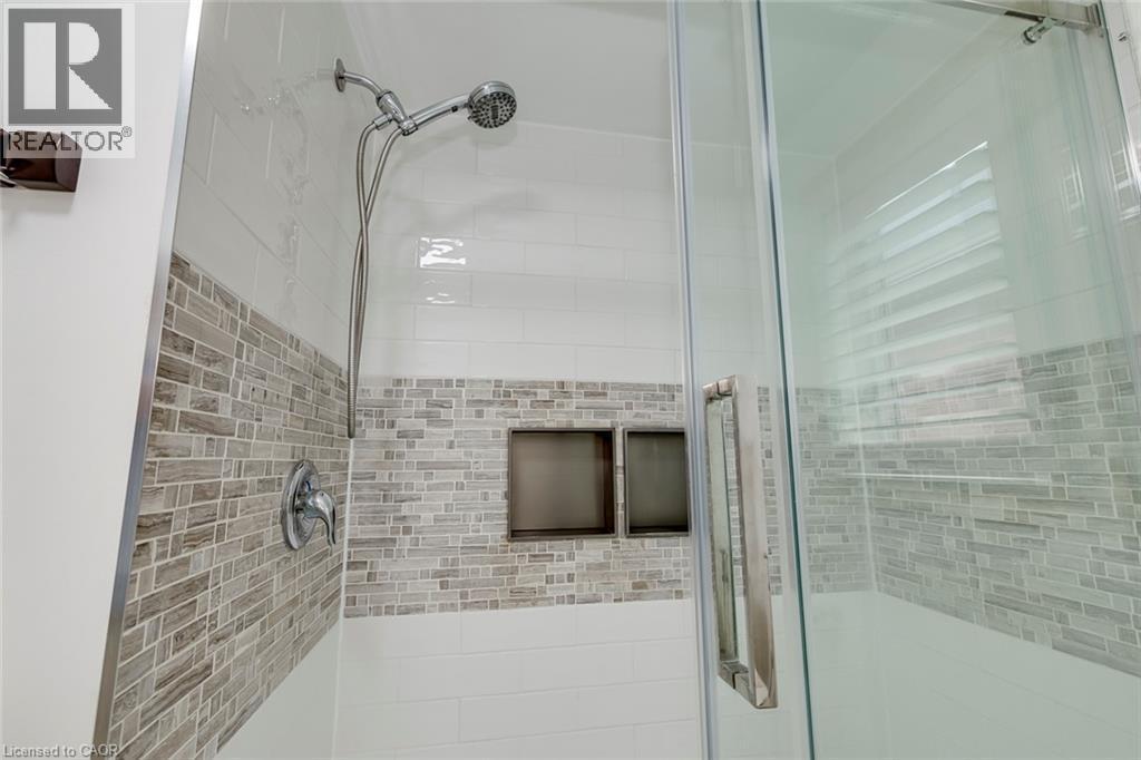 Glass-enclosed shower featuring white subway tile, a mosaic tile accent band, dual recessed shower niches, a handheld shower fixture, and a single-handle temperature control - 598 Bessborough Drive, Milton, ON - Indoor Photo Showing Bathroom
